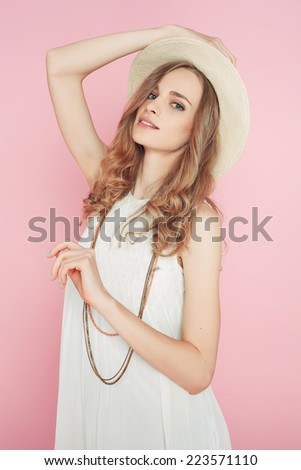 Beautiful young woman in hat white dress posing on pink background