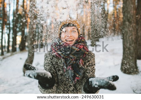 Young hipster woman in winter forest having fun with snow falling in hands