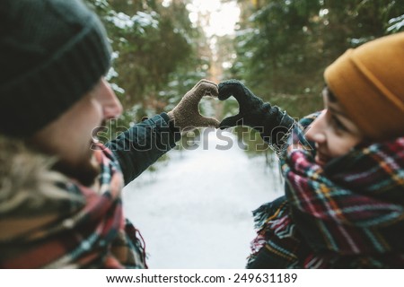 Young hipster couple holding hands in love heart symbol in winter forest