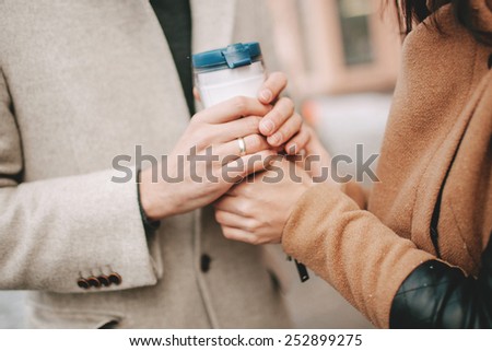Man holds a coffee cup and the hands of the woman in winter outdoors