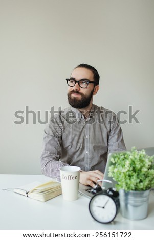 Busy man with beard in glasses thinking over laptop with coffee on the table