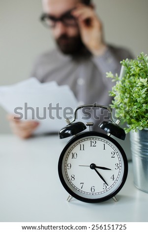 Busy man with papers over the table with alarm clock and laptop