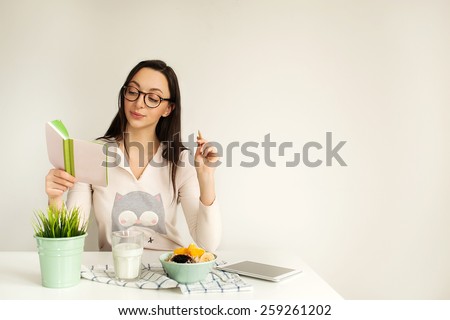 Woman in glasses making notes in notepad with porridge, milk and tablet on table, copy space