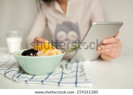 Woman making notes in notepad with porridge, milk and tablet on table