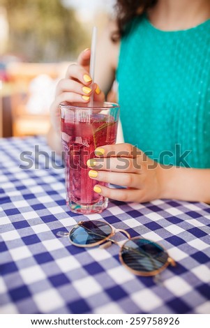 Hands of woman holding a tube in glass of red cocktail on table