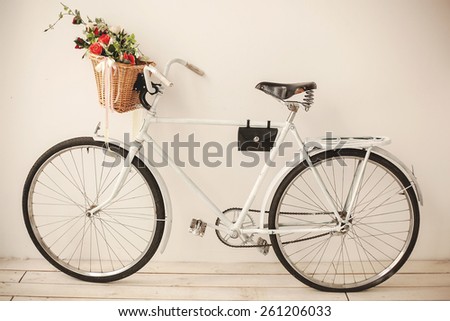 White retro bicycle on white wooden floor with basket full of flowers