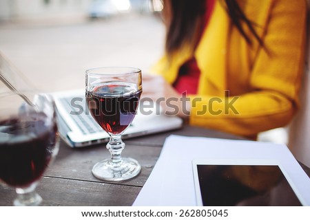Woman works with glass of red wine tablet and laptop in street cafe