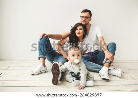 Young hipster father, mother and cute baby boy sitting on rustic wooden floor over white background