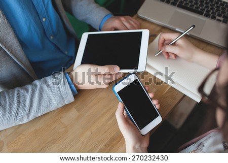 Smartphone, tablet and laptop with notepad in hands of man and woman on the table in cafe