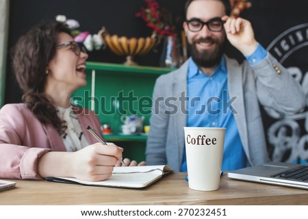 Young hipster man with woman in glasses collaborating in cafe using laptop, tablet, smartphone and coffee