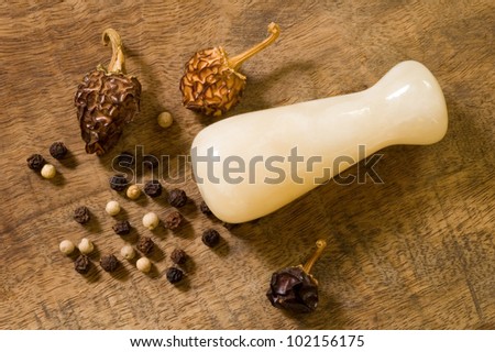 Black peppercorns, dried red peppers and a pestle on a vintage cutting board
