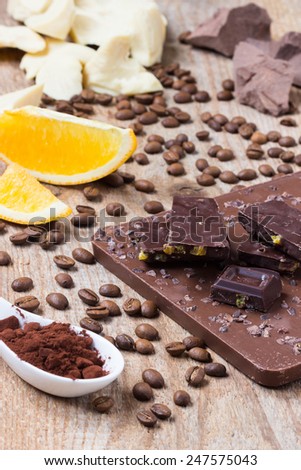 Raw chocolate with orange, cacao and coffee nibs on black background, coconut oil and cocoa mass, selective focus