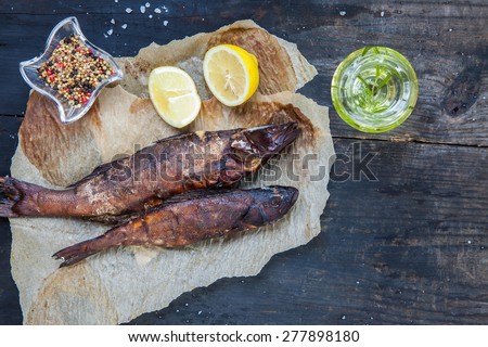 Smoked perch with lemon slices on black wooden background