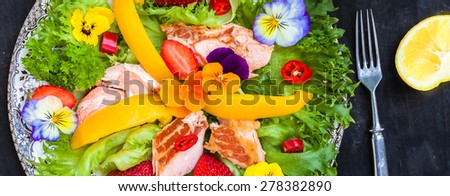 Salad with smoked salmon, strawberries and edible flower on black wooden background, top view