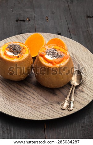 Baked pumpkin with cheese, rice and chia seeds on wooden plate, black wooden background, selective focus