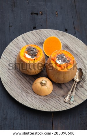 Baked pumpkin with cheese, rice and chia seeds on wooden plate, black wooden background, selective focus