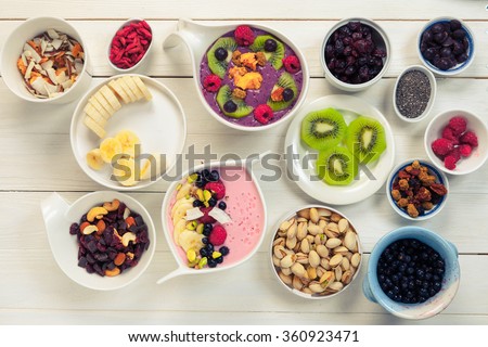 Decorating of Pink strawberry and blue acai berries smoothie bowl with superfood ingredients, Clean eating breakfast concept, top view, white wooden table, rustic style