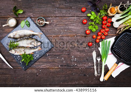 Fresh fish with aromatic herbs, spices, salt, bottles with olive oil and balsamic vinegar,perch on slate tray on a wet dock, on dark vintage background, top view, healthy food, diet or cooking concept