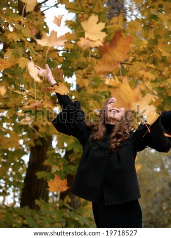 Young beauty girl throws leaves upwards in autumn forest.