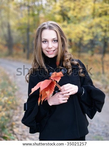 Portrait of a pretty smiling girl with leaves in fall forest