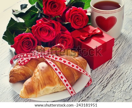 Romantic breakfast with tea in cups, croissants, gift box and rose
