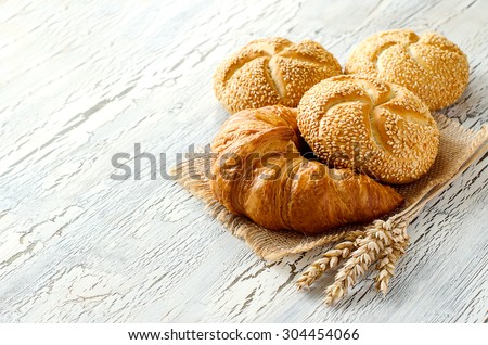 Croissant and small loaf with sesame, ears of wheat, baked bread on sackcloth, bakery concept, copy space white background