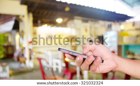 Mobile held in hand with Coffee shop blur background