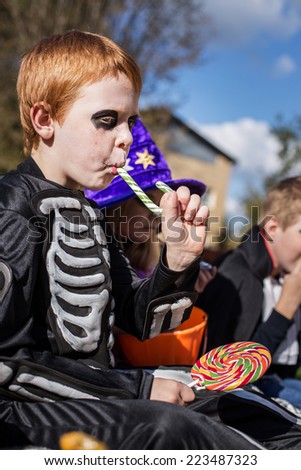Red haired child with skeleton costume eating colorful candy. Halloween. Outdoor portrait