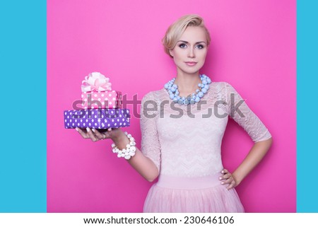 Beautiful young woman with cream colored dress holding pink and purple gift boxes. Studio portrait over bright pink background with blue edge