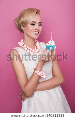 Nice blonde woman holding cake with candle. Birthday, holiday. Studio portrait over pink background
