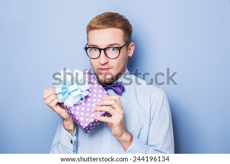 Young man with a wrapped gift box. Present, birthday, Valentine. Studio portrait over blue background