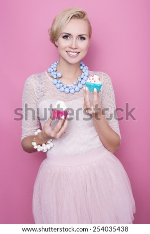 Cute young women hold colorful sweets. Soft colors. Studio portrait over pink background
