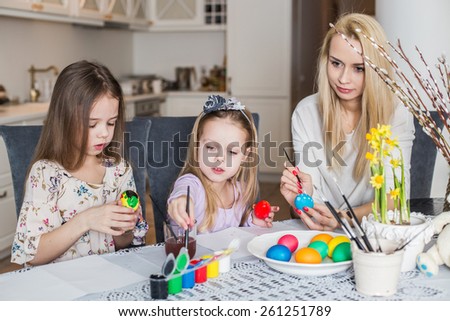 Young mother and her two daughters painting Easter eggs. Cozy home atmosphere. Easter