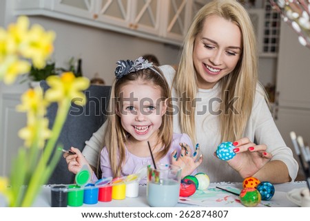 Happy mother and daughter painting easter eggs in the living room. Easter, family, holiday and child concept