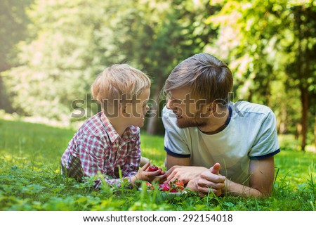 Summer photo happy father and son together lying on green grass. Life moment family resting on the nature