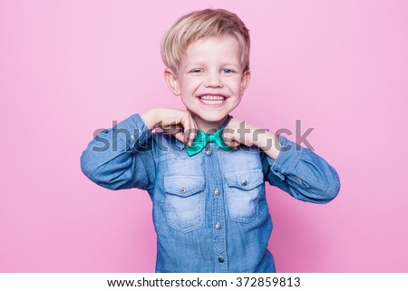 Young handsome kid smiling with blue shirt and butterfly tie. Studio portrait over pink background