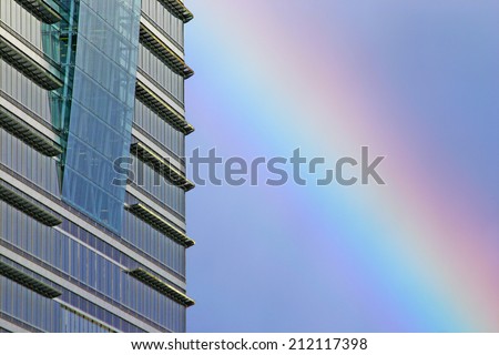 Business rainbow. Detail of a contemporary London skyscraper reflecting the blue sky with a natural rainbow visible in the background.