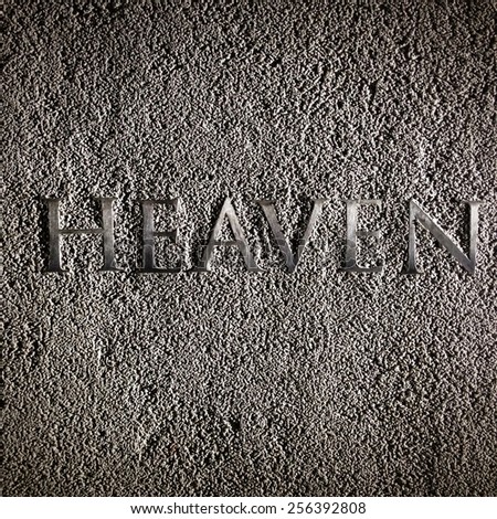 Heaven. The word 'heaven' engraved into coarse concrete with harsh side lighting and high contrast shadows.
