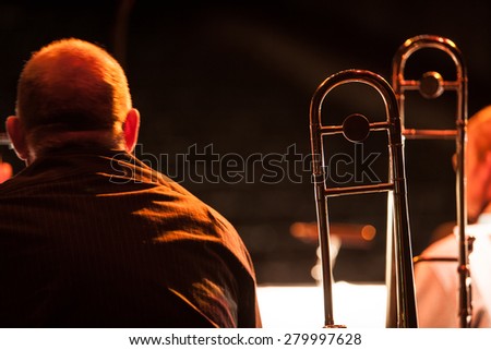 A solitary trombonist from a traditional big band jazz ensemble with his instrument beside him waiting to begin playing.
