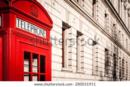 Traditional old-style UK red phone box set against a beige government building in central London.