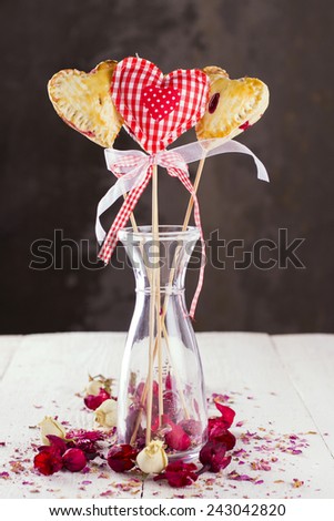 Cookies pops in the form of heart and heart from fabric in a pattern a red cage with buds of roses