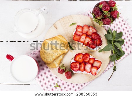 Sandwich with strawberry, fried bread, strawberry, milk in jug and glass on white wooden table - top view