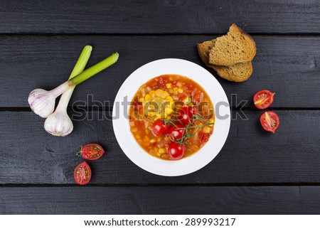 Corn soup with cherry tomatoes in white plate on wooden background with garlic and bread. Top view