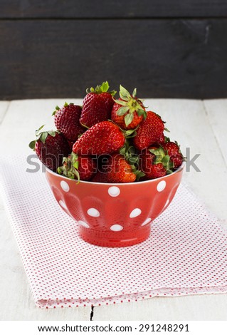 Strawberry in red bowl with a pattern in peas on fabric napkin on a white table