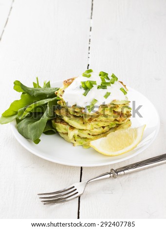Zucchini fritters on white plate with sour cream, spinach and lemon on white background