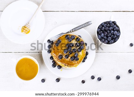 Heap of pancakes watered with honey and blueberry on a white wooden table the top view