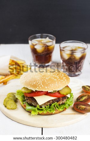 Burger with meat, lettuce, tomatoes, cheese, pickles, onions, french fries and sparkling water on a white wooden background