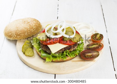 Burger with meat, lettuce, tomatoes, cheese, pickles, onions on a white wooden background