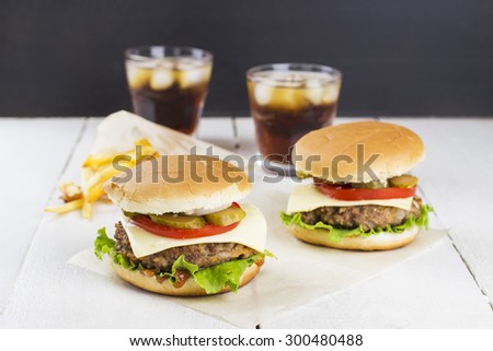 Two mini burgers with meat, lettuce, tomatoes, cheese, pickles, onions, French fries and sparkling water on a white wooden background