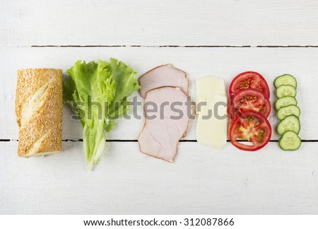 Ingredients for sandwich: lettuce, bacon, tomatoes, cucumber, cheese on a white wooden background
